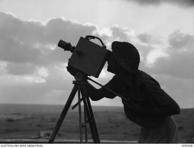 Tobruk, Libya. 1941-08. Damien Parer, a Department of Information photographer, filming with a Newman-Sinclair 35mm camera, probably the Auto Kine Camera model, during the Siege of Tobruk. Parer could be filming material for the Department of Information production, Siege of Tobruk. (See AWM Film F01097)